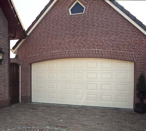 Habitat cassette avec une grande porte de garage sectionnelle blanche en pvc installée sur une maison individuelle en brique pour particuliers.