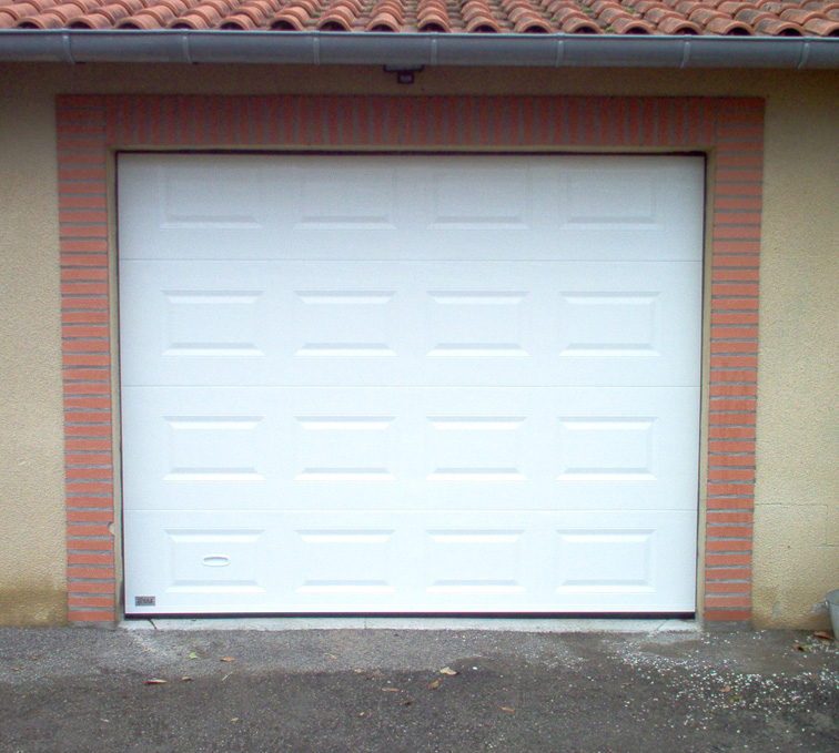 Habitat cassette automatique avec porte de garage sectionnelle blanche en pvc et ses contours en brique sur une maison pour particuliers.